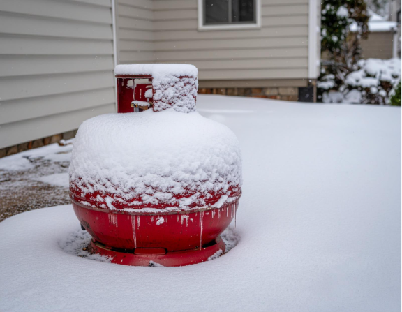 Propane tank covered in snow during winter, showing the importance of regular seasonal maintenance.