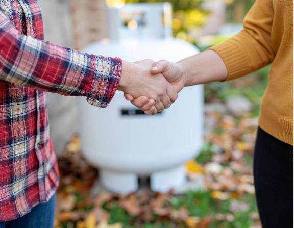 Two people shaking hands outdoors with a propane tank in the background, symbolizing reliable service.
