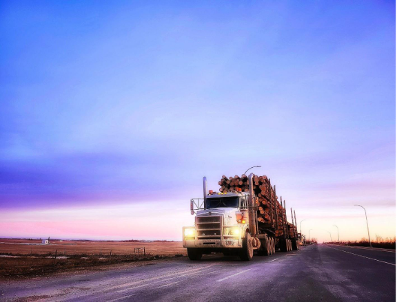 A tractor trailer hauling a large load of lumber down the highway, showcasing the type of heavy-duty equipment that relies on off-road diesel for power, hauling capacity, and consistent performance. The image highlights the vehicle, cargo, and roadway setting to illustrate real-world applications of diesel fuel in commercial transport.